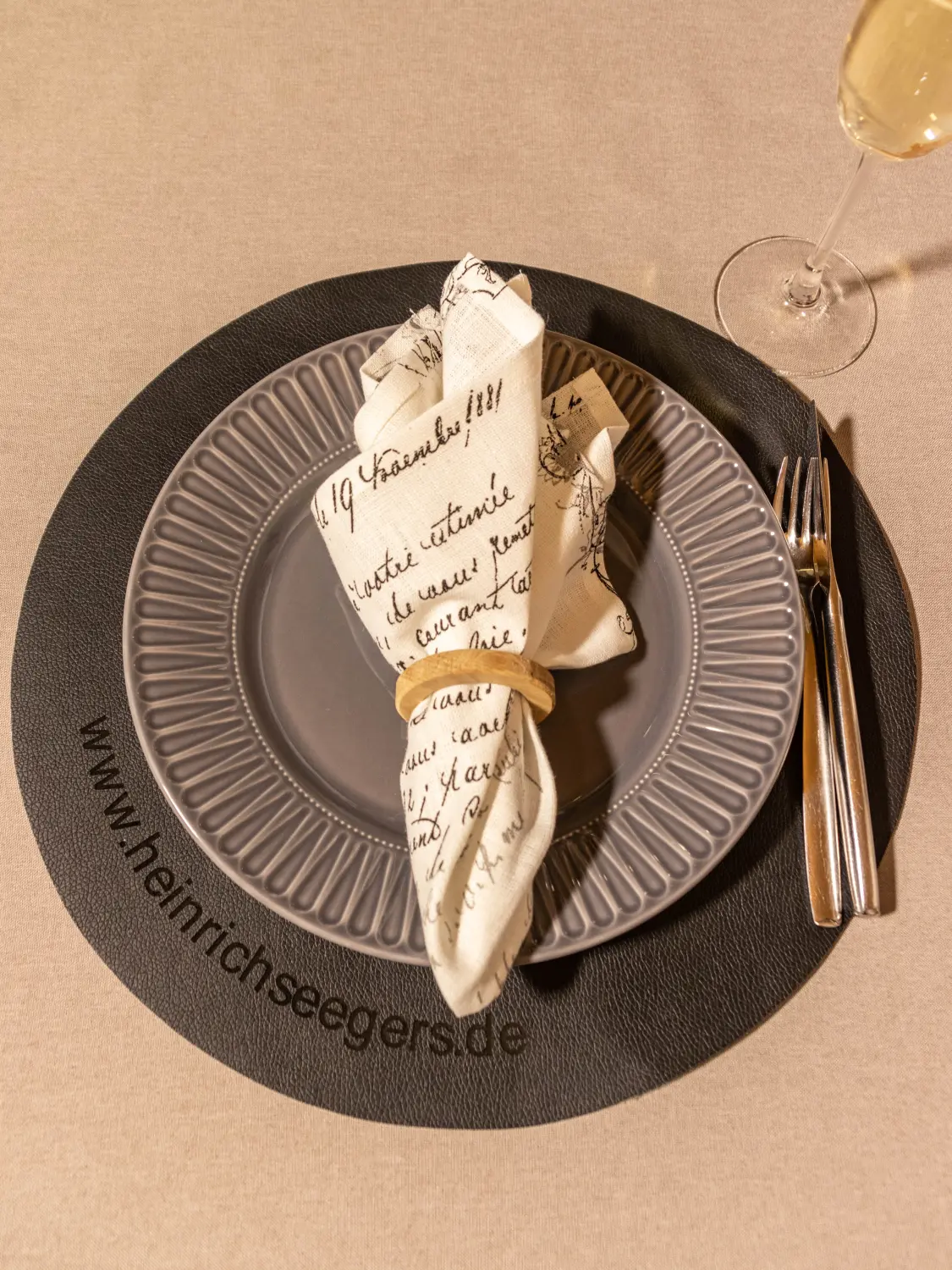 IKEA SVARTVIDE Tischset, ein grauer Teller mit Reliefmuster, eine Serviette mit handgeschriebenem Text und Besteck von Heinrich Seegers Objekttextilien GmbH